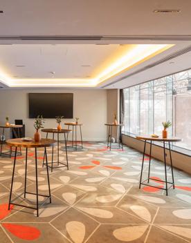 The Wellington room at InterContinental has one wall of windows, patterned carpet, and several tall tables dotted around the room.