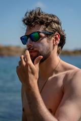 A shirtless man wearing sunglasses applying Seasick Sunscreen to his face.