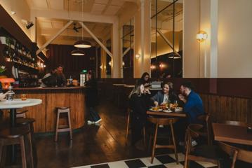 Three people are sitting at a table in the Ram, while staff works behind the counter.