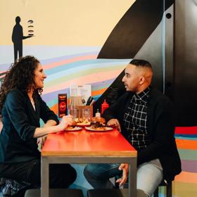 Two friends sit at a high-top table enjoying burgers, beers and good conversation.