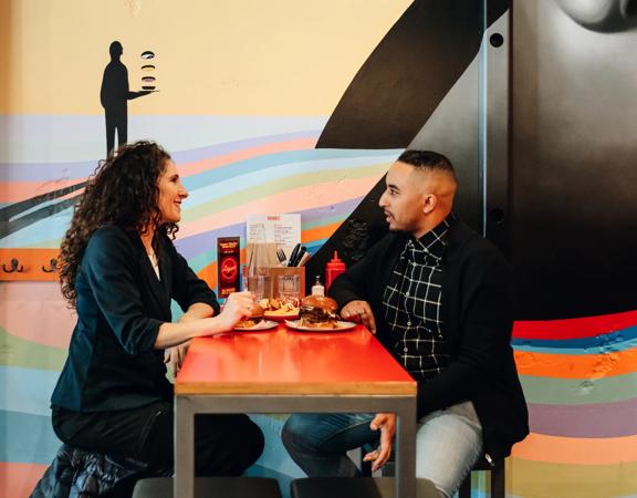 Two friends sit at a high-top table enjoying burgers, beers and good conversation.