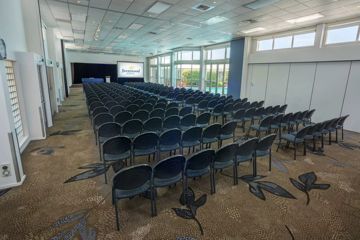 Long rectangle shaped room with over 100 chairs facing towards a projector at the front of the room.