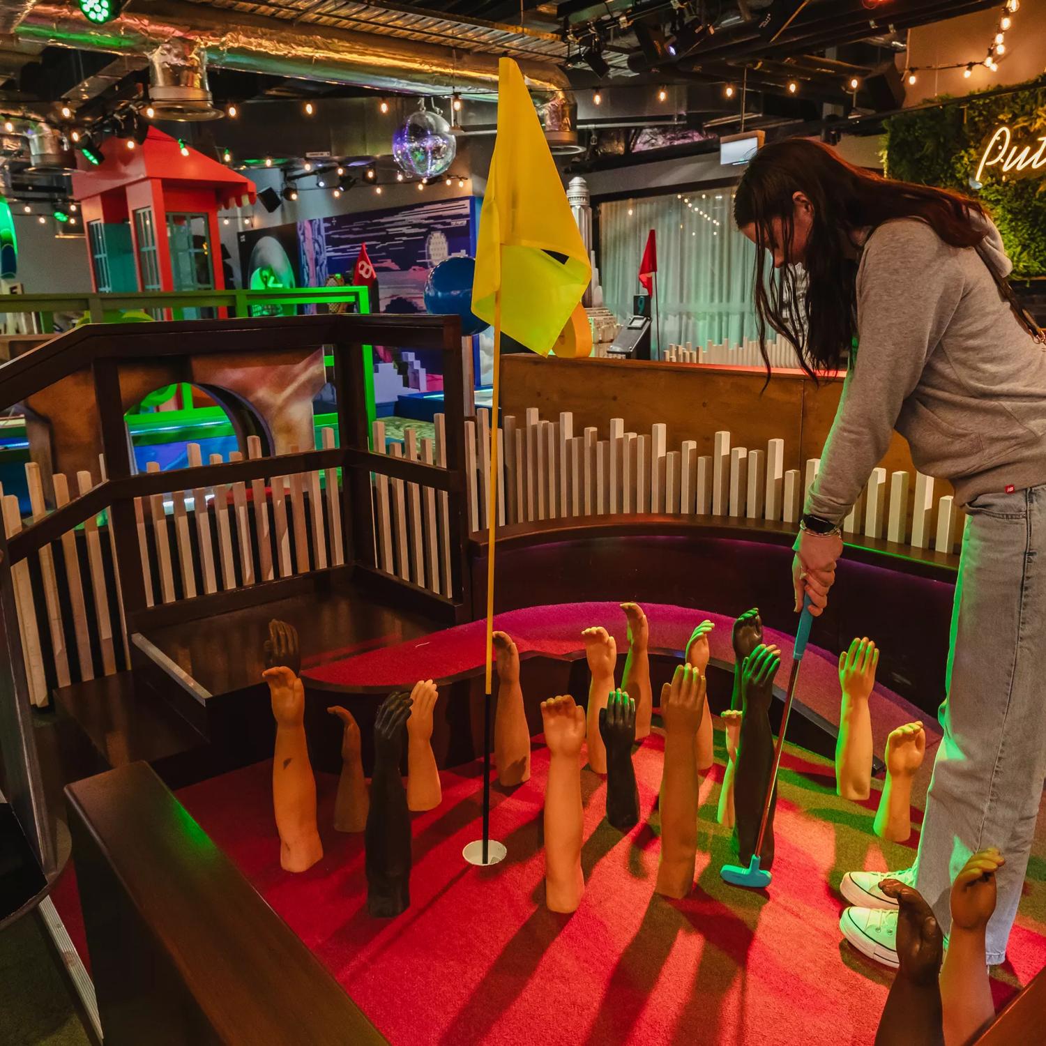 The interior of Holey Moley, the mini golf course and bar in Willis Lane, located at 1 Willis Street in Wellington. A person puts on a course with mannequin arms fixed to the felt floor reaching upward as an obstacle around the whole. 