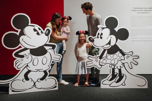 A family of four poses for a photo with two life-size cut-outs of Mickey and Minni Mouse at the Disney: The Magic of Animation exhibition.