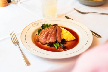 A plate with a sliced steak, jus, mashed potatoes and broccolini.