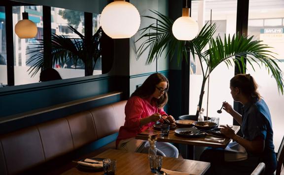 2 customers eating at a table in Koji, lantern lights hang above them and a fern sits to their left.