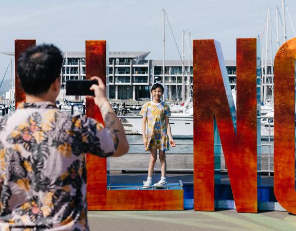 A parent taking of a photo of their child posing in the Well_ngton sign on the waterfront.