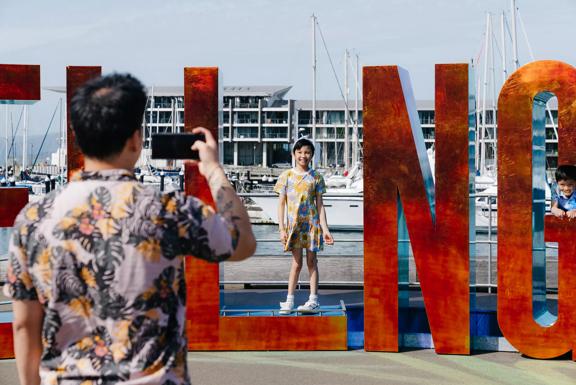 A parent taking of a photo of their child posing in the Well_ngton sign on the waterfront.