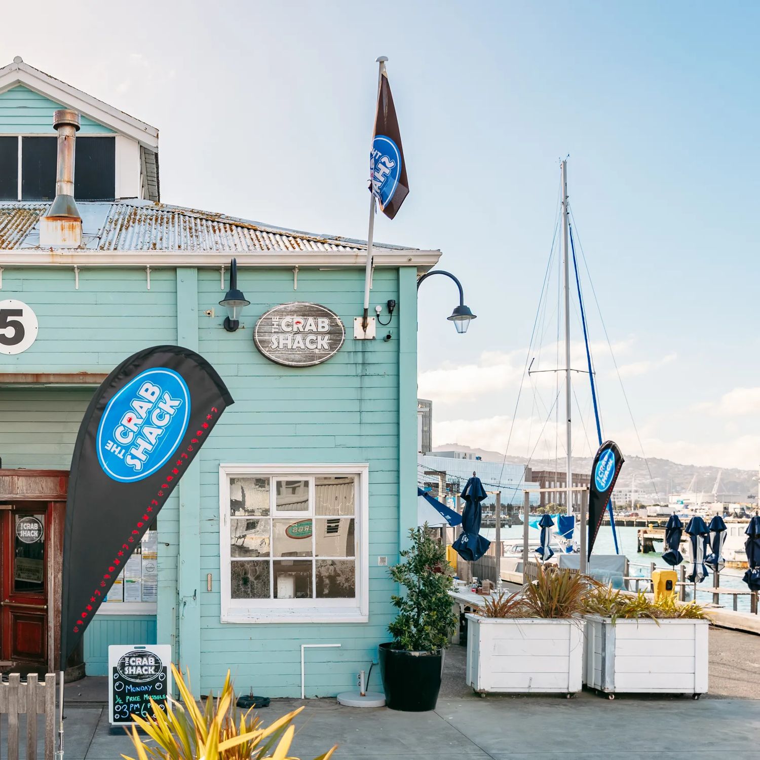 The turquoise exterior of The Crab Shack on Queens Wharf. In the background is the Wellington harbour.