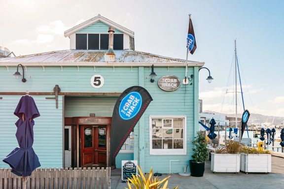 The turquoise exterior of The Crab Shack on Queens Wharf. In the background is the Wellington harbour.