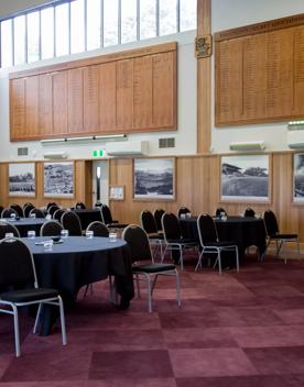 The Norwood Room at the Basin Reserve filled with circular tables with black tablecloths surrounded by chairs. Black and white photos of the grounds line the walls.