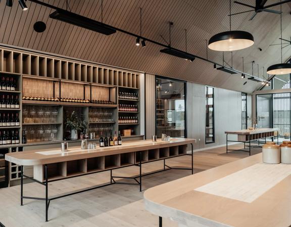 A room inside The Runholder with a wall cabinet full of wine. The floor, walls, and high-ceiling roof are a light wood with black accents in the lights and fixtures.