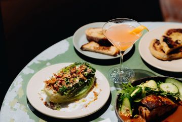 A table with a cocktail in a martini glass and four plates of food.