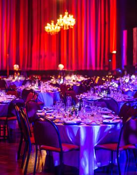 A banquet set up at the Michael Fowler Centre for the Becca Ball. The round tables are covered in shiny table cloths, reflecting the purple lighting.