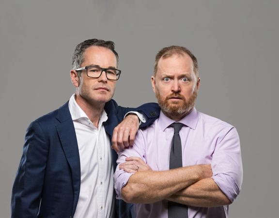 Two office workers pose in front of a grey background.