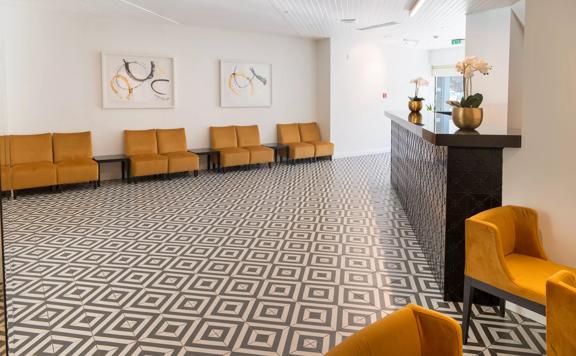 Inside the open, minimal-styled lobby at Bay Plaza Hotel, with white walls, turmeric-coloured chairs and a tiled floor.