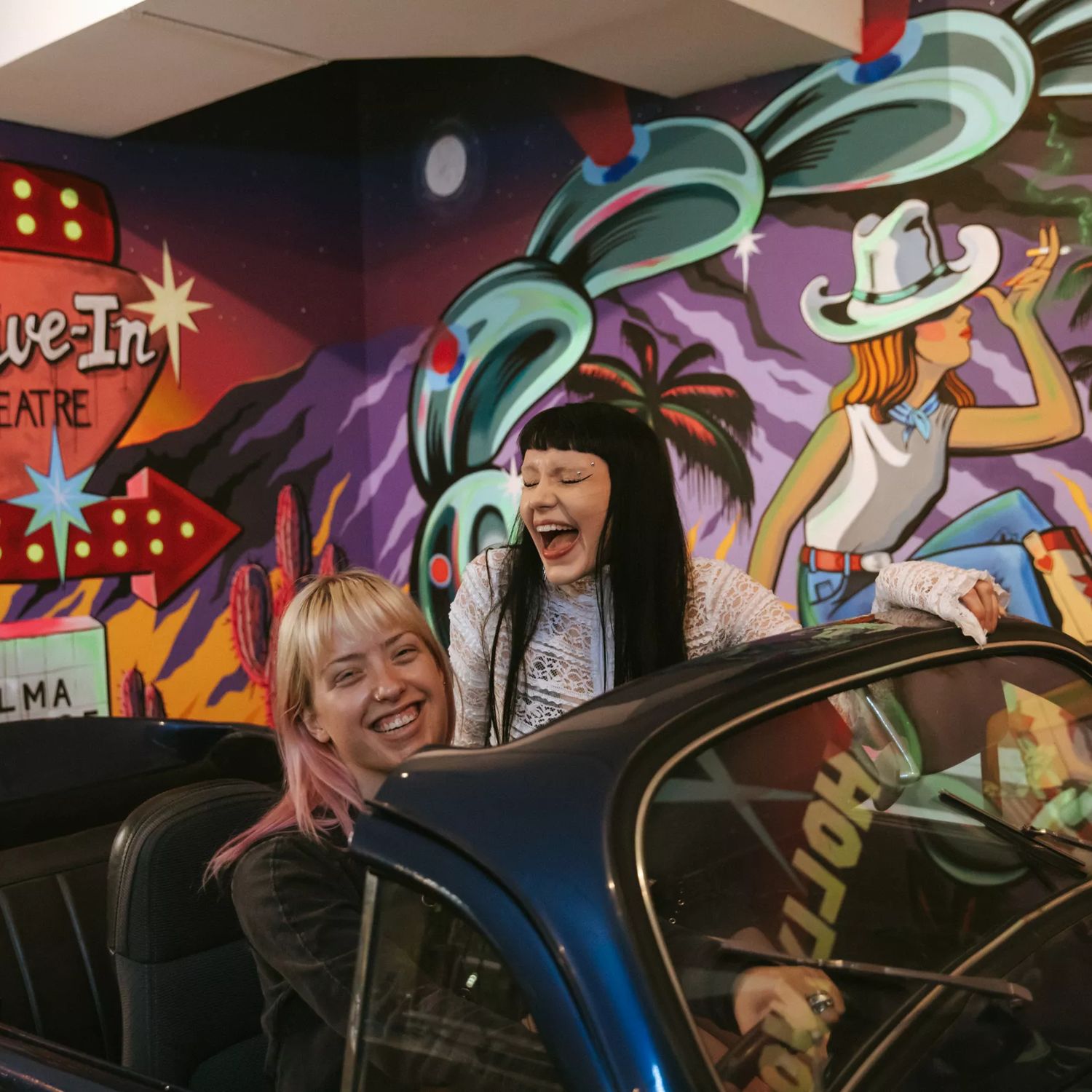 Two people pose for a photo in a convertable car inside Bizarre Bazaar.
