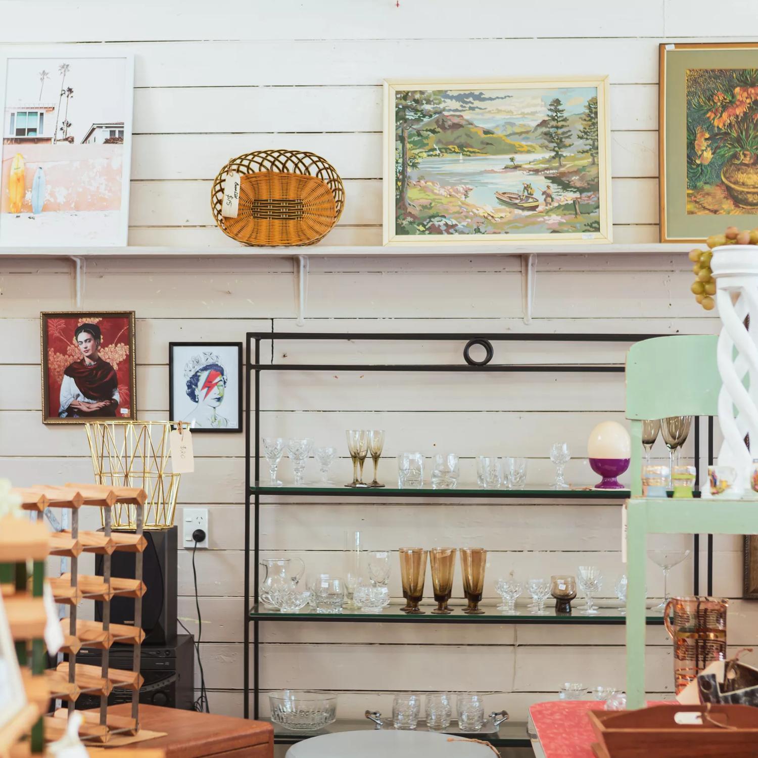 Shelves of second-hand items line the wooden white wall at Petone Treasures. There's glassware, pictures, and furniture.