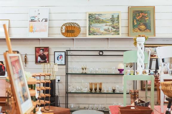 Shelves of second-hand items line the wooden white wall at Petone Treasures. There's glassware, pictures, and furniture.