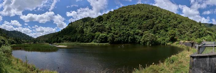 A lake and a small tree-covered under a blue cloudy sky.