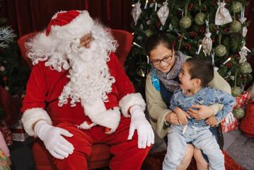 A small child sitting on his mother's lap is elated to meet Santa Claus.