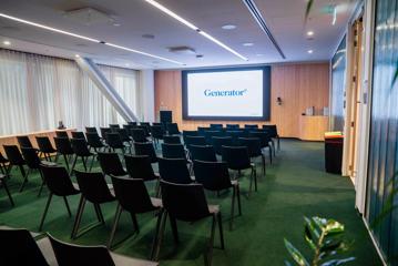 The Pūtahi room at Generator Bowen Campus is set up in a theatre style with many black chairs facing a projector screen.