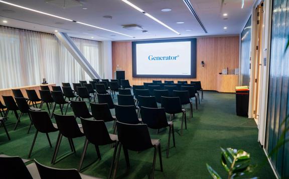 The Pūtahi room at Generator Bowen Campus is set up in a theatre style with many black chairs facing a projector screen.