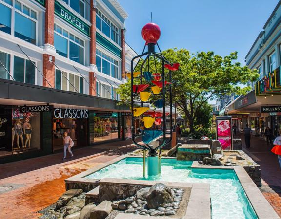 People walking down Cuba Street, past the Bucket Fountain, an iconic kinetic sculpture.