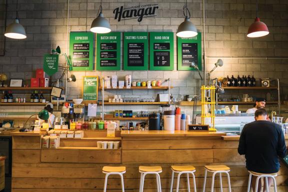 The front counter at The Hangar, made of wood with wooden stools and green menu boards on the wall, underneath their logo.