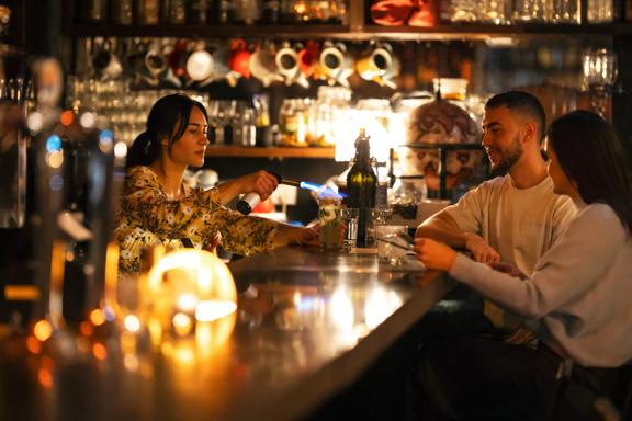 The interior of The Library, a cocktail bar on Courtney Place in Te Aro, Wellington. The bartender is using a flame to toast the garnish on a drink while two patrons are sitting at the bar.  