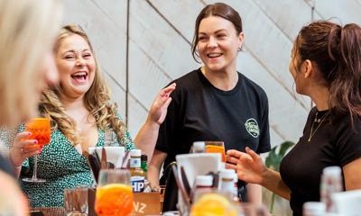 Three people chat and laugh while sipping on mimosas at brunch.