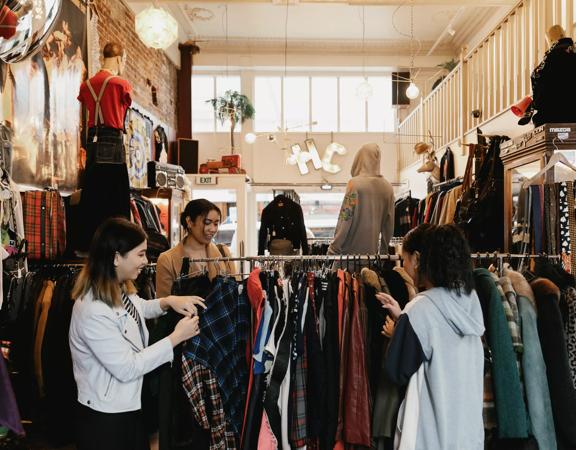 The interior of Hunters & Collectors, a vintage clothing store in Te Aro, Wellington. Three shoppers are looking through the items on a clothing rack. 