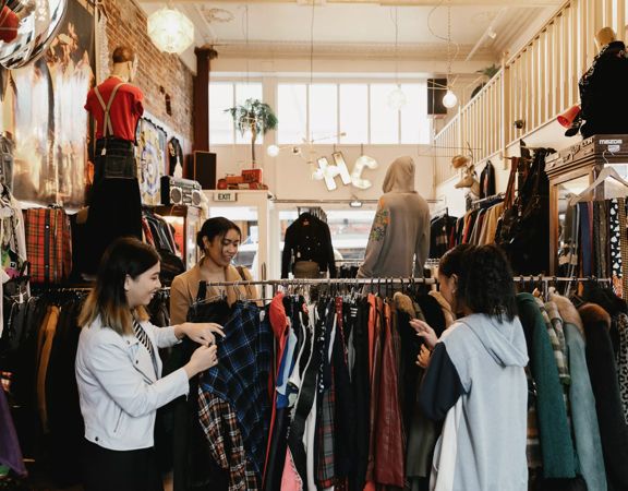 The interior of Hunters & Collectors, a vintage clothing store in Te Aro, Wellington. Three shoppers are looking through the items on a clothing rack.