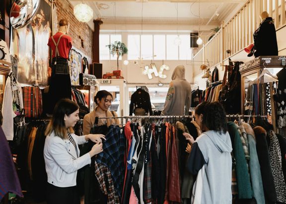 The interior of Hunters & Collectors, a vintage clothing store in Te Aro, Wellington. Three shoppers are looking through the items on a clothing rack.