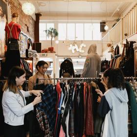 The interior of Hunters & Collectors, a vintage clothing store in Te Aro, Wellington. Three shoppers are looking through the items on a clothing rack. 