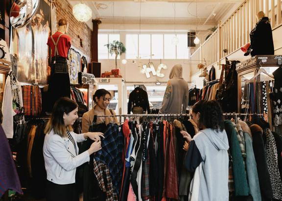 The interior of Hunters & Collectors, a vintage clothing store in Te Aro, Wellington. Three shoppers are looking through the items on a clothing rack. 