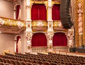 Inside St James Theatre in Wellington, New Zealand. There are four balcony box seating with red curtains to the right of the stage and decorative structural columns.