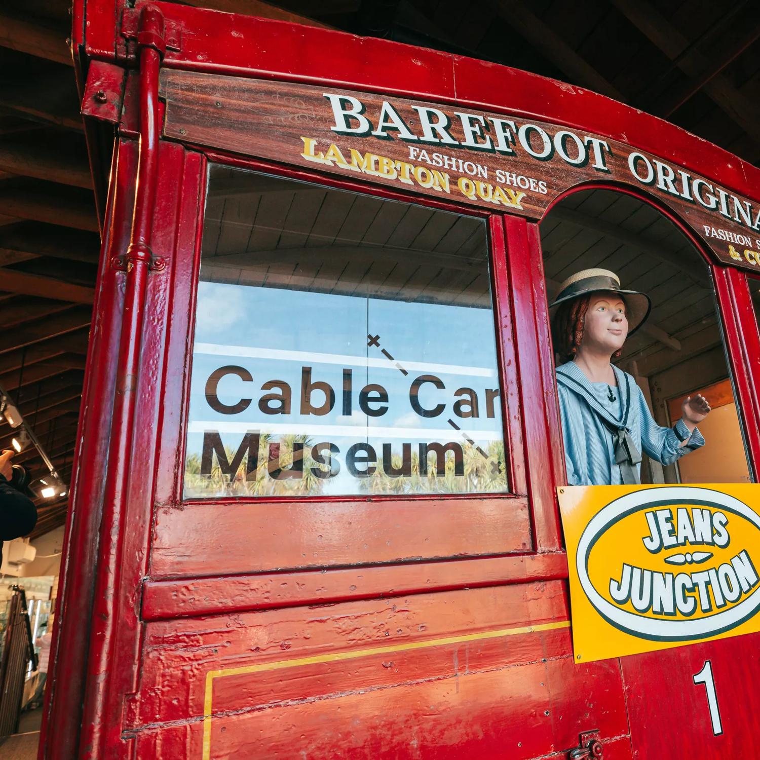 The backside of a life-size model of an old cable car at the Cable Car Museum in Kelbunr, Wellington with a mannequin figure waving out the window.