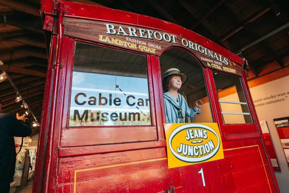 The backside of a life-size model of an old cable car at the Cable Car Museum in Kelbunr, Wellington with a mannequin figure waving out the window.