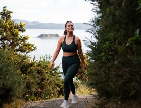 A person walking up the Bus Barn Track in East Harbour Regional Park. Behind them, the Wellington Harbour fills the background with blue.