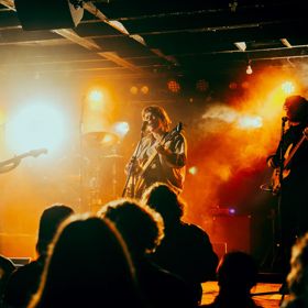 A band performs under spotlights and fog machines at a crowded music venue.