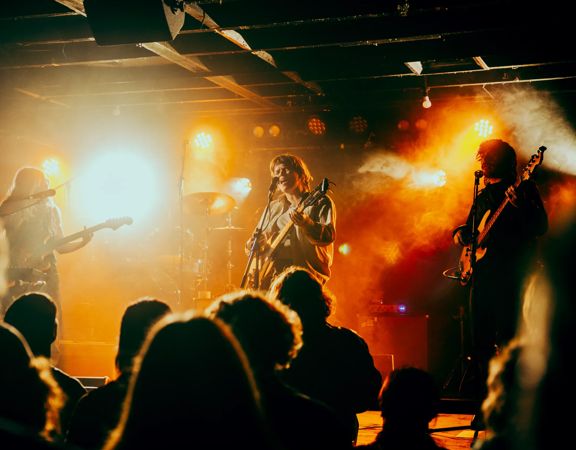 A band performs under spotlights and fog machines at a crowded music venue.
