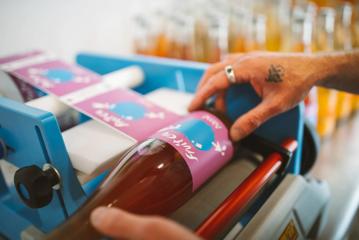 A person uses a label machine to apply a sticker to a bottle of Frui Cru.