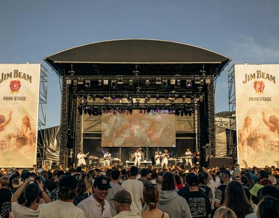 Seven musicians perform on The Park Stage at Jim Beam Homegrown, a New Zealand music festival on Wellington's waterfront to a packed audience. 