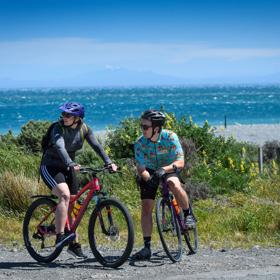 2 people on bikes stopped next to a beach on the Wainuiomata Connector Ride.