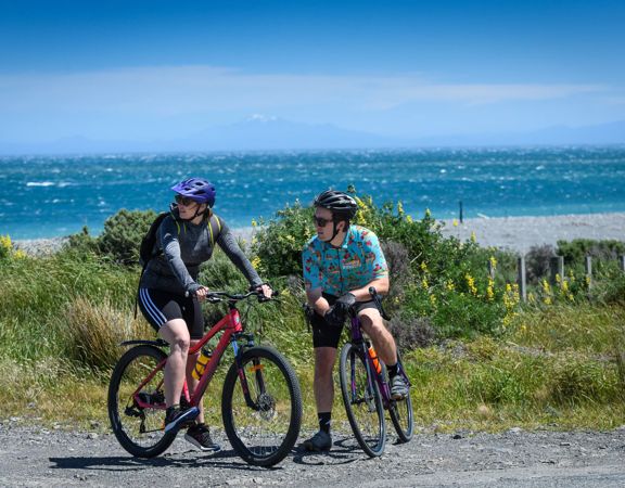 2 people on bikes stopped next to a beach on the Wainuiomata Connector Ride.