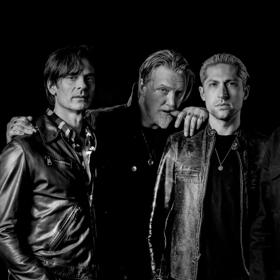 The five band members of Queens of the Stone Age stand with cool and serious facial expressions. 