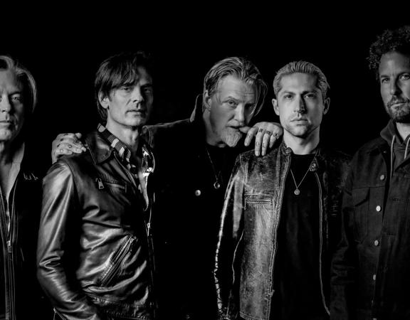 The five band members of Queens of the Stone Age stand with cool and serious facial expressions. 