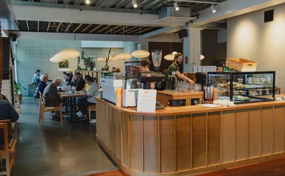 The front counter at Twenty Eight Cafe, located at 28 Cornwall Street in Lower Hutt, with two people working and customers enjoying food and drinks in the background.