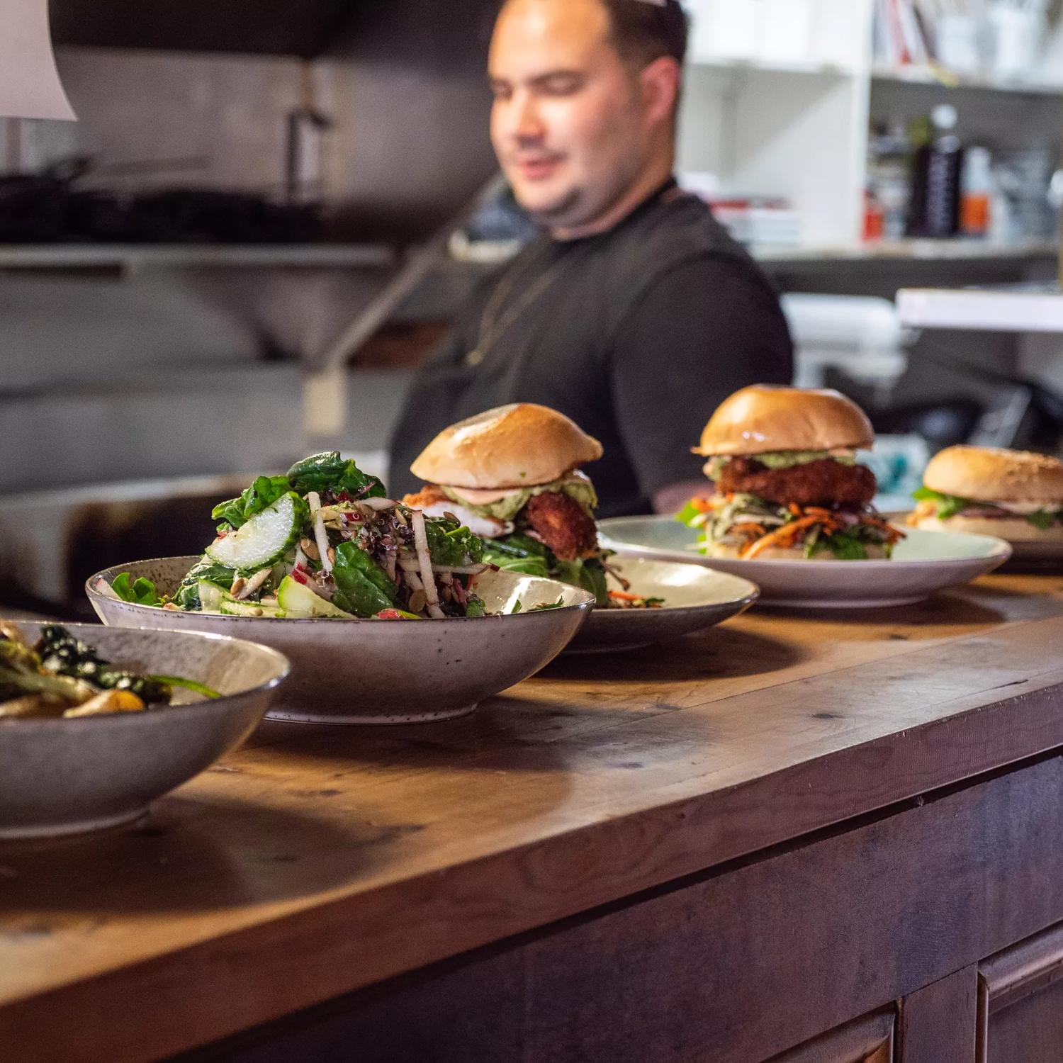 5 dishes from Raumati Social Club served on the bar, with the Chef standing behind.